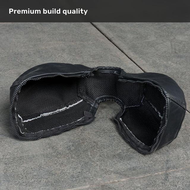 A Bells of Steel Kettlebell Wrap in black, featuring visible stitching and a breathable mesh interior for style and floor protection, rests on a gray stone surface. The corner caption reads, “Premium build quality.”.