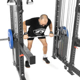 A man uses THE KOLOSSOS - Smith Functional Trainer by Bells of Steel for a bent-over barbell row. He's in a black T-shirt and shorts, with a weightlifting belt. A plain white background accentuates his focus and determination.