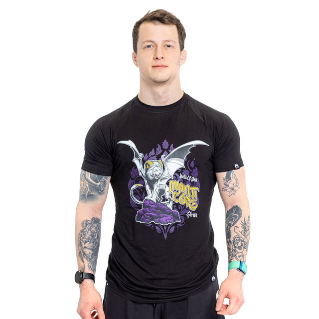 A person is wearing a Bells of Steel Bamboo T-Shirt in black, adorned with a white dragon-like creature and purple floral design. They have tattoos on their arms and are standing against a plain white background.