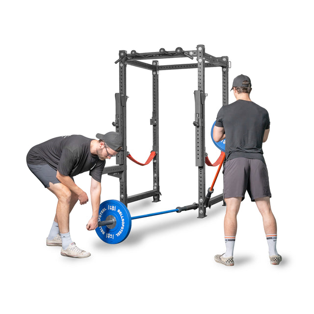 Two individuals in matching black athletic wear set up a Bells of Steel Landmine Rack Attachment with blue weights, preparing for an intense workout.