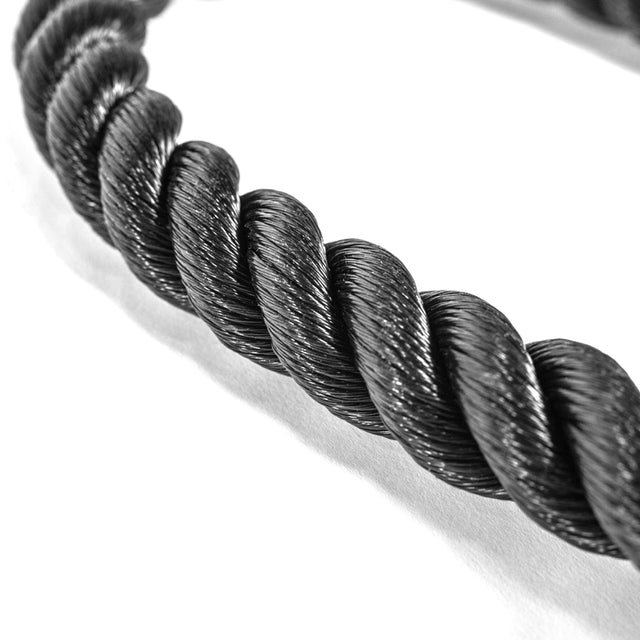 Close-up image of the Bells of Steel Tricep Rope Extension, a thick, twisted black rope with a shiny texture. Coiled on a white surface, it showcases its sturdy braided design, ideal for cable machines targeting tricep exercises.