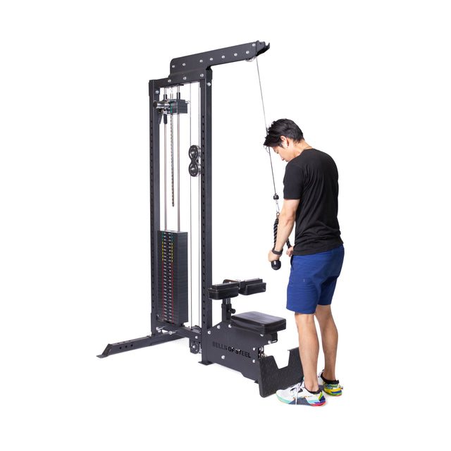 A person exercises on a tall cable machine, expertly using the Bells of Steel Tricep Rope Extension. The weight stack is on the left, with their focus entirely on targeting their triceps. Wearing a black t-shirt, blue shorts, and multicolored shoes, they stand confidently against a white background.