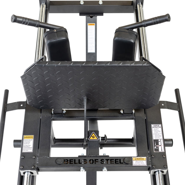 Close-up of a Bells of Steel Leg Press Hack Squat Machine with pads, handles, warning labels, and a diamond plate design. This machine is perfect for versatile strength training exercises, such as hack squats and leg presses. Ideal sled capacity makes it great for home gym use.