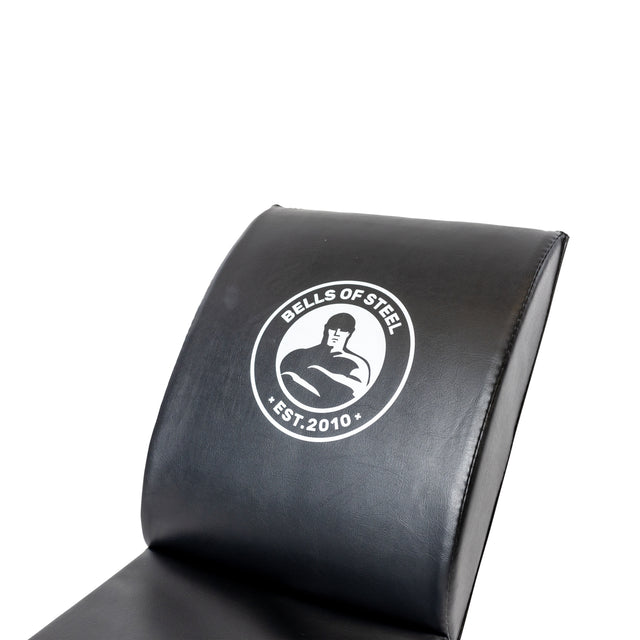 The Luxury Sit Up Mat by Bells of Steel, featuring a black design with a white logo and "Est. 2010," mimics lumbar curvature for enhanced comfort, similar to using a gym bench during workout sessions.