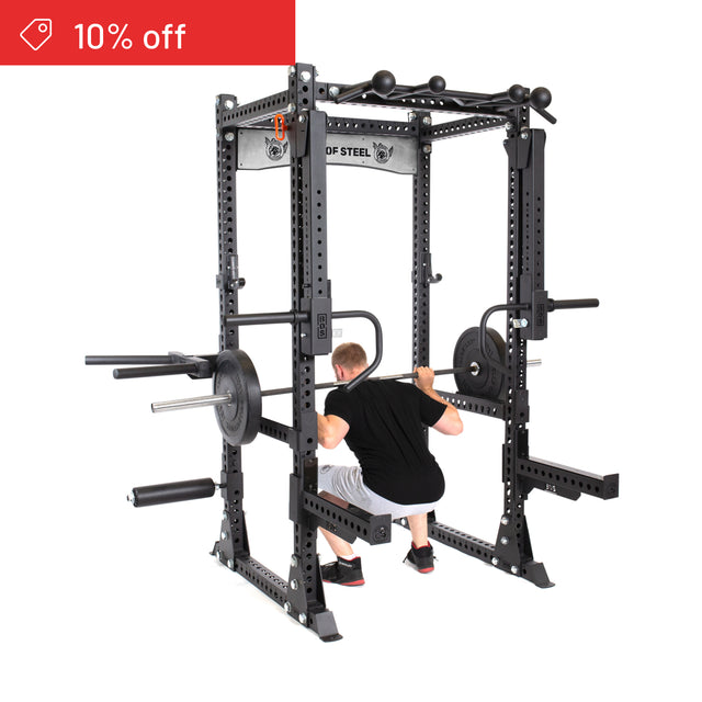 Wearing gym clothes, a person performs a barbell squat inside the Bells of Steel Manticore Flat Foot Power Rack Builder (3" x 3", 1" Holes), with weights. A red banner in the top left shows "10% off," ideal for any home gym.