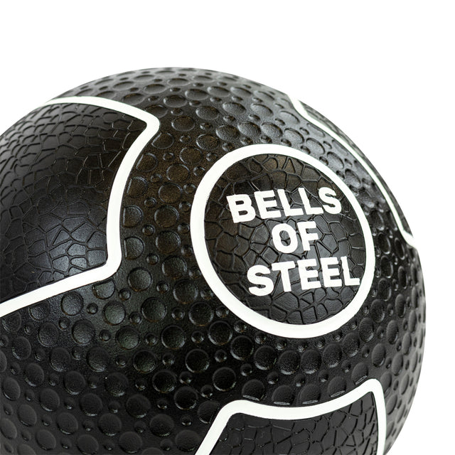 The textured black Mighty Grip Medicine Balls by Bells of Steel feature raised white "BELLS OF STEEL" lettering and outlined sections, offering a superior grip that effortlessly enhances your fitness routine.