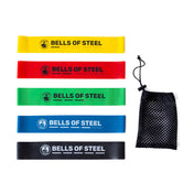 A set of five Mini Bands, made from high-grade latex in colors yellow, red, green, blue, and black, are displayed vertically and labeled with the "Bells of Steel" brand. To their right is a black mesh drawstring bag.