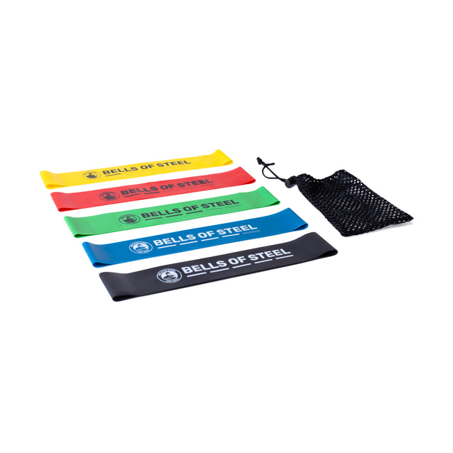 A set of five Bells of Steel Mini Bands, crafted from high-grade latex in the colors yellow, green, red, blue, and black, are displayed horizontally alongside a black mesh carrying pouch on a white background.