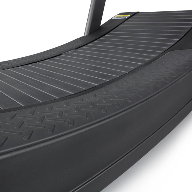 Close-up of the Blitz Magnetic Resistance Manual Treadmill by Bells of Steel, showcasing its black textured running surface and curved design. This sleek manual treadmill enhances cardio workouts with its modern appearance and magnetic resistance feature.