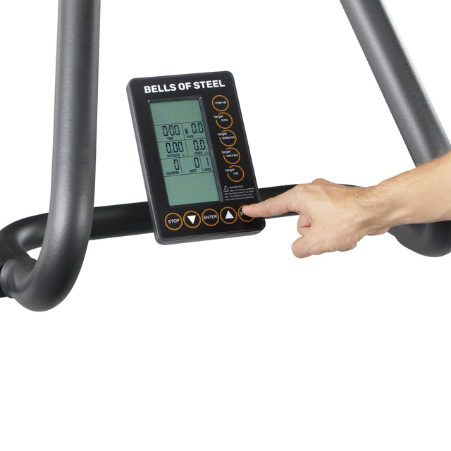 A hand presses a button on the Bells of Steel Blitz Magnetic Resistance Manual Treadmill display, showcasing various controls and a digital screen with cardio metrics. Black bars frame the display against a white background, emphasizing its magnetic resistance feature.