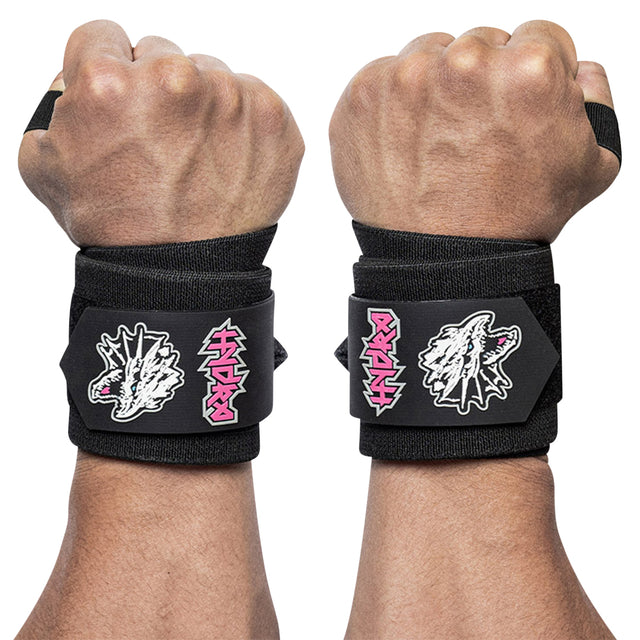 Two forearms display the Mighty Wrist Wraps from Bells of Steel in black, secured with Velcro closures ideal for powerlifting. These competition-style wraps are adorned with striking pink and white graphic designs featuring a jagged logo and a roaring dinosaur head, set against a plain white background.