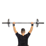 A man in a black shirt lifts a barbell overhead against a white background, wearing Bells of Steel Mighty Wrist Wraps for enhanced wrist support.