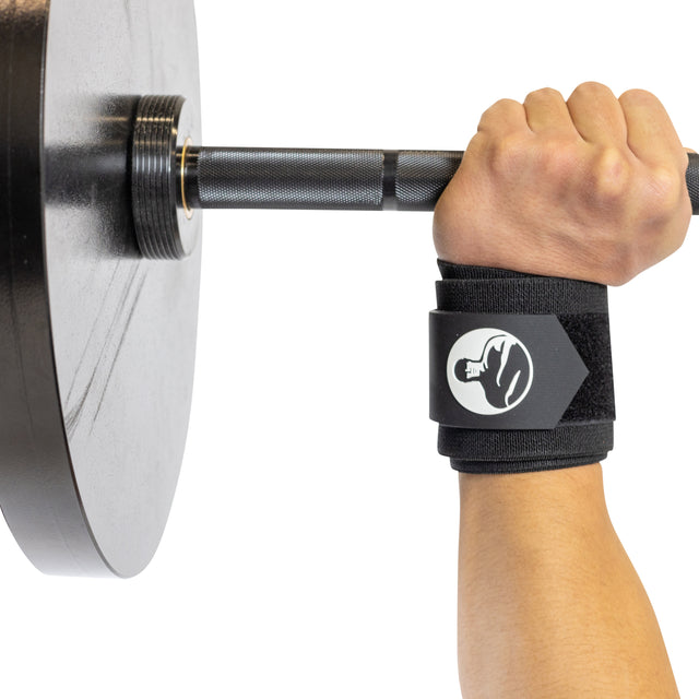 A person’s hand grips a barbell with Bells of Steel's Mighty Wrist Wraps, featuring a fist logo. The barbell is loaded with a large, round black weight plate, highlighting powerlifting essentials against a plain white background.