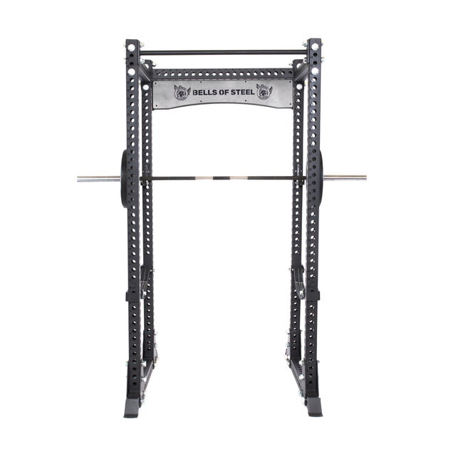 The Manticore Flat Foot Power Rack Builder by Bells of Steel securely holds a durable barbell set on its solid hooks. Made from black metal featuring multiple 1-inch adjustment holes, it proudly displays the brand's logo at the top. This versatile setup is ideal for intense workouts, set against a plain white background.
