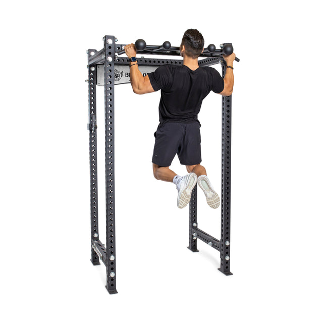 A person in a black shirt, black shorts, and white sneakers performs a pull-up on the Bells of Steel Globe Pull Up Bar, a metal bar with multiple grip options for strength training, isolated on a white background.