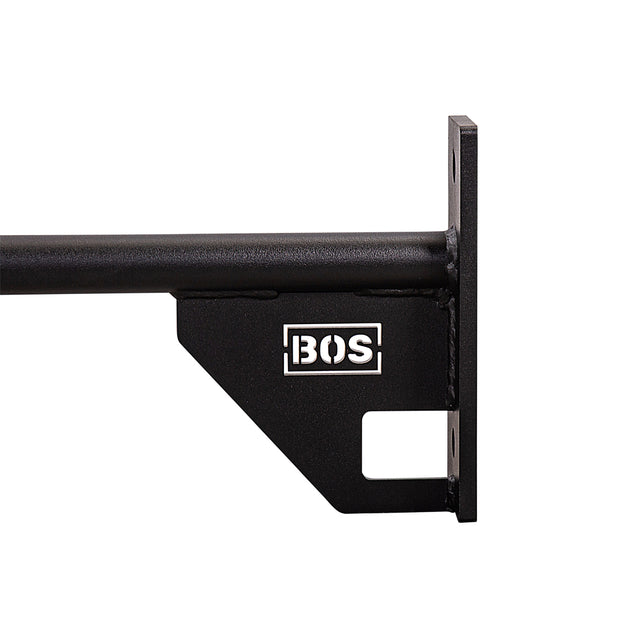 An up-close view of a black, wall-mounted 70" Pull Up Bar by Bells of Steel is shown. The bar features a rectangular rust-resistant metal plate, with the letters "BOS" displayed in white and includes a distinctive cutout shape on the bottom right corner. The pull-up bar extends horizontally from the wall.