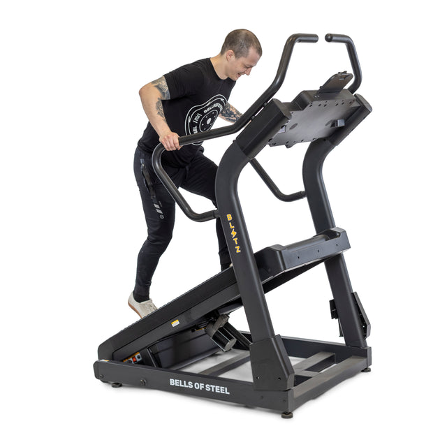 Clad in black exercise gear, a person intensely works out on a Bells of Steel Blitz Mountain Climber Treadmill, gripping the side rails and channeling their energy into the session.