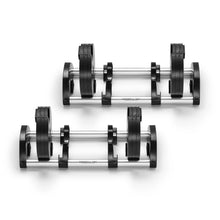Two Nuobell adjustable dumbbells with black weight plates and chrome handles rest side by side on matching chrome and black stands against a white background. Perfect for strength training, these dumbbells are compatible with the NÜOBELL 50 to 80 LB Expansion Kit - Standard (Chrome).