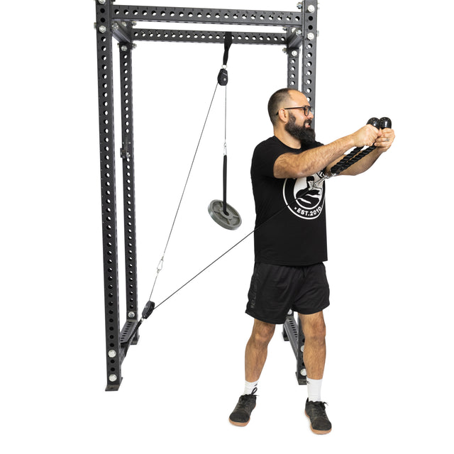 Someone in a black shirt and shorts is using the Bells of Steel Tricep Rope Extension, focusing on their triceps by holding the cables with both hands extended in front in a gym setting.