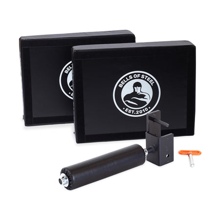 A gym equipment set from Bells of Steel's Hydra Nordic Curl Package that includes two black foam plyo boxes with the brand logo, a padded foot holder for Nordic hamstring curls, and an orange L-shaped tool.