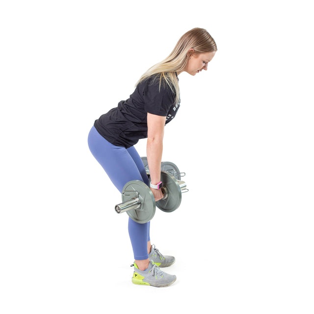 A woman is performing a deadlift with a Bells of Steel Loadable Dumbbell Handle. She bends at the hips with slightly bent legs, maintaining a firm grip on the gym equipment. Dressed in a black shirt, blue leggings, and gray sneakers, she stands against a white background.