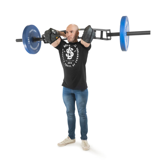 A person in a black T-shirt, jeans, and beige shoes is lifting a Bells of Steel Omni Bar fitted with blue weights. They appear engaged in exercise, gripping the barbell's knurling with both hands against a plain white backdrop.