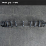 An overhead view of the Bells of Steel Arch Nemesis Swiss Bar—a specialty barbell with three angled grips—rests on a gray tiled floor, labeled "Three grip options" to showcase its versatility as a cable attachment.