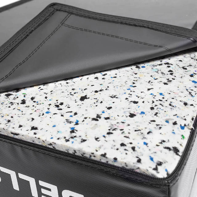 A close-up of a Deadlift Pad by Bells of Steel shows a corner folded back to reveal the speckled foam interior. The black surface has white text along the edge, while the foam features blue, black, and white flecks for enhanced durability and style.