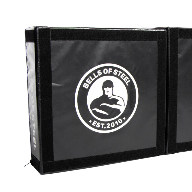 The Deadlift Platform Drop Pad Pair from Bells of Steel Canada is a black mat featuring a logo in the center that illustrates a stylized muscular figure alongside the text "BELLS OF STEEL EST. 2010." This mat is equipped with a velcro seam along the edge, designed to absorb impact and protect floors during intense workouts.