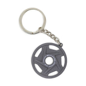 The Plate Keychain by Bells of Steel is perfect for fitness enthusiasts, featuring a miniature weight plate with "BELLS OF STEEL" and "1.5 lb" inscribed on it. Its sleek, dark design, attached to a silver chain and keyring, makes it an ideal gift or promotional item for your social media followers.