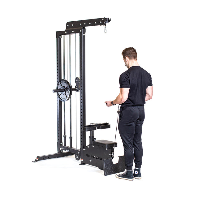 Dressed in black, a person stands before the Bells of Steel Lat Pulldown Low Row Machine, a home gym equipment with adjustable weights and a seated pulley system featuring a high pulley attachment, seemingly ready to exercise.