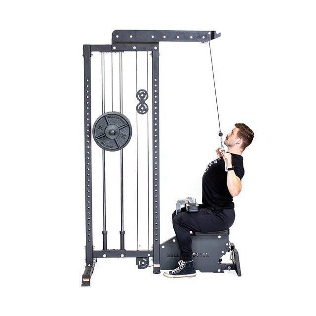 Dressed in black, an individual uses the Bells of Steel Lat Pulldown Low Row Machine in their home gym, pulling the bar down to their chest with focused precision and relying on the machine's weight stack for resistance during the exercise.