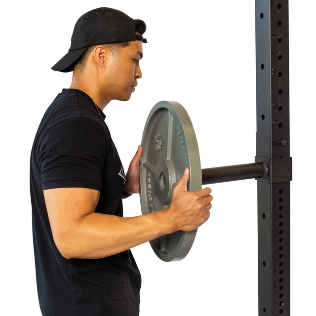 A person in a black shirt and cap loads Bells of Steel Pin Plate Pegs onto a power rack's barbell.