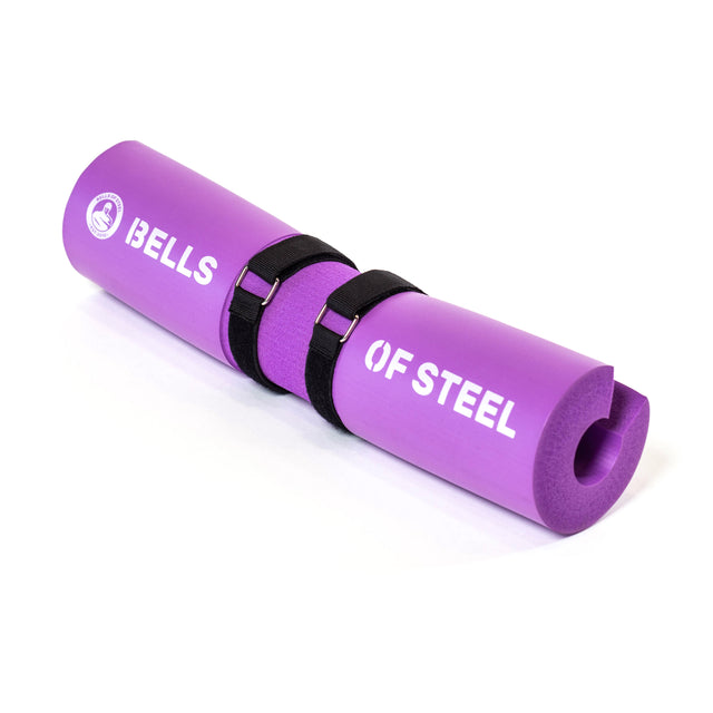 The purple Barbell Pads with Straps by Bells of Steel feature foam construction, an ergonomic central groove, adjustable black straps for secure attachment, and branding printed on the pad for comfortable weightlifting exercises.