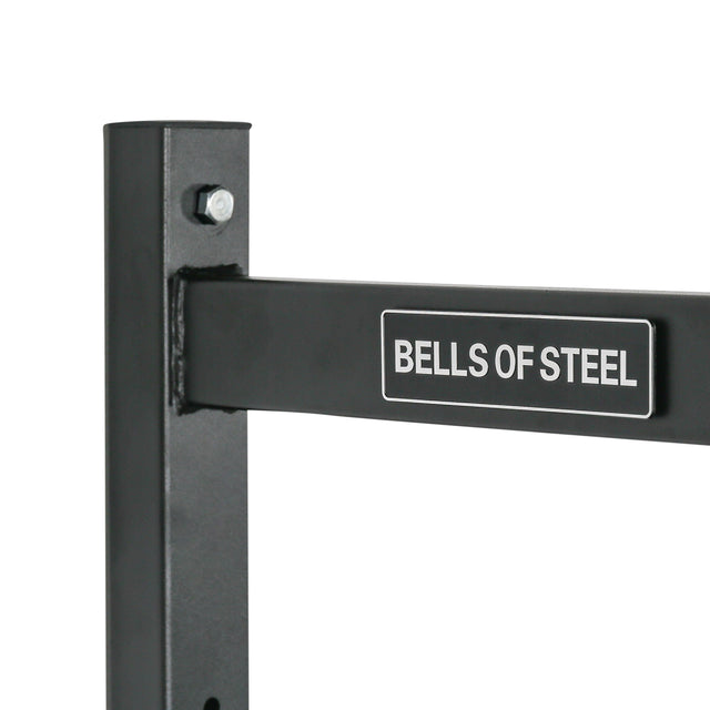 A close-up shows the Bells of Steel Adjustable Wall or Ceiling Mounted Pull Up Bar's black metal frame with a rectangular multipurpose bar and logo, secured by a metal bolt. It is perfect as a ceiling-mounted pull up bar, contrasting against the plain white background.