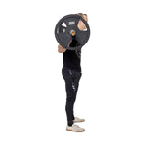 Against a white background, a person in a black t-shirt and dark pants performs a back squat using Bells of Steel's Rubber Coated Iron Weight Plates. There are two weight plates on each side of the barbell.