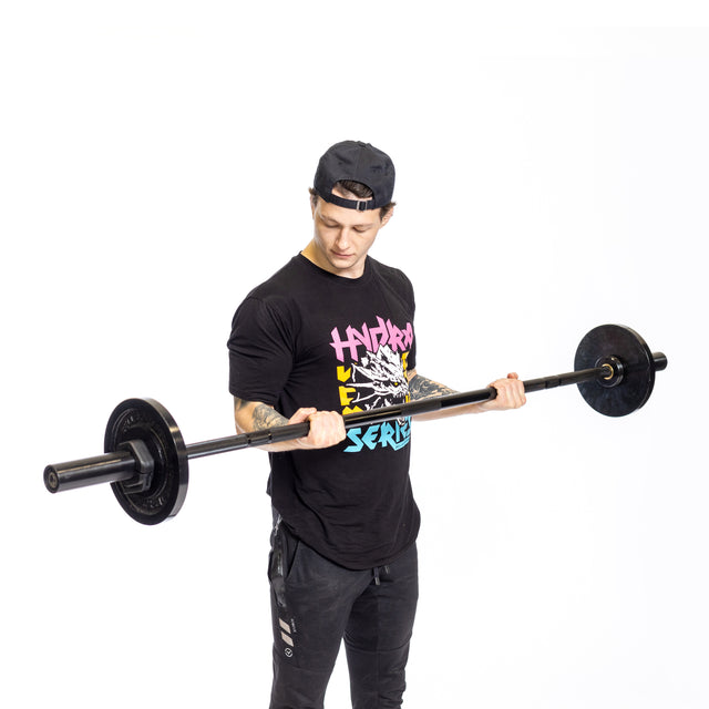 A person in a black cap and colorful t-shirt intently lifts the Bells of Steel Short Rackable Barbell, with a durable black zinc coating, in a compact home gym against a plain white background.