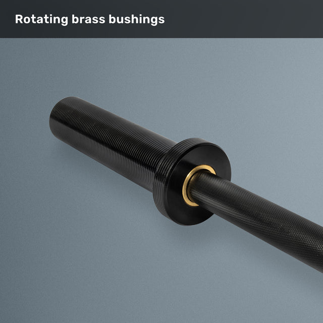 A close-up of the Bells of Steel Short Rackable Barbell with rotating brass bushings, set on a gray surface. The text “Rotating brass bushings” appears at the top, emphasizing the durable design of this 69-inch barbell—an ideal choice for any compact home gym.