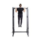 A man in black athletic wear performs a pull-up on the Bells of Steel Residential Power Rack (2.3" x 2.3", ⅝" holes), isolated on a white background.