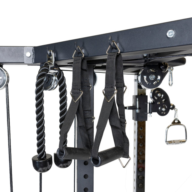 Close-up of Bells of Steel's All-in-One Trainer, featuring a gym cable machine with various attachments like black straps with handles, a tricep rope, and a single handle. Integrated pulleys enhance the metal frame's function as a versatile trainer for diverse workouts.