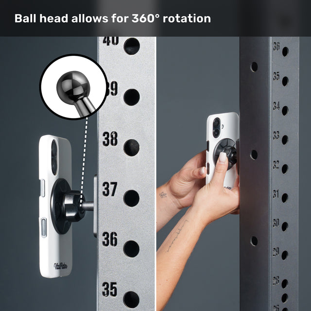 A hand attaches a smartphone to a metal rack using the Bells of Steel Selfie Sentinel - Magnetic Rack Phone Holder, demonstrating its MagSafe-compatible magnetic mount with a 360-degree rotating ball head. An inset provides a close-up view of the ball head mechanism.