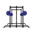 Displayed is a Hydra 2-Sided Rack by Bells of Steel, a squat rack featuring two blue weight plates on each side with white lettering. The image reveals a clear front view of this versatile and open ecosystem fitness equipment.