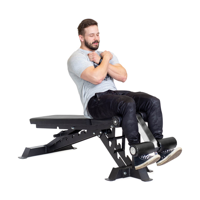 A man wearing a gray t-shirt and black pants does sit-ups on the Bells of Steel Buzz-Saw Heavy-Duty Adjustable Bench, using its leg support and adjustable back pad angles, set against a pristine white background.