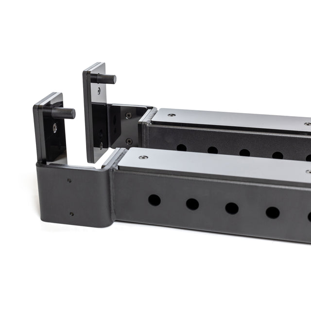 Two black metal Bells of Steel Flip-Down Safeties gym rack attachments with multiple adjustment holes and hooks are shown close-up on a white background, designed for training safety and to support weights or bars on a power rack.
