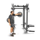 A man in athletic gear stands beside the Bells of Steel Shoulder Boulder/Chest Fly Attachment, adjusting weights on its space-saving rack. The versatile gym equipment includes various exercise attachments, and he appears focused on achieving that coveted V-taper look.