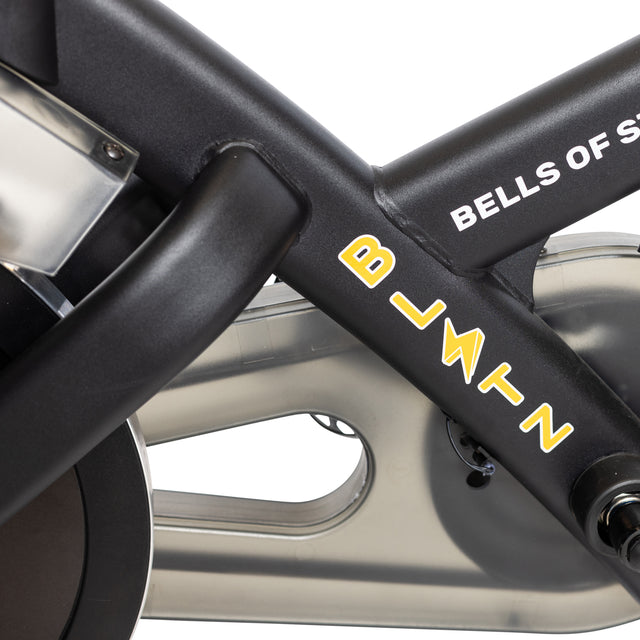 Close-up of the Blitz Indoor Cycling Bike's sleek black frame with "BELLS OF STEEL" and "BLITZ" in vibrant yellow and white. The design reveals the flywheel and adjustable handlebars, emphasizing its premium magnetic resistance system.