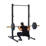 In their home gym, a person in athletic clothing performs a squat using the sleek Hydra Squat Stand Builder with 3" x 3" tubing and ⅝" holes by Bells of Steel, showcasing the versatility of its modular design for effective workouts.