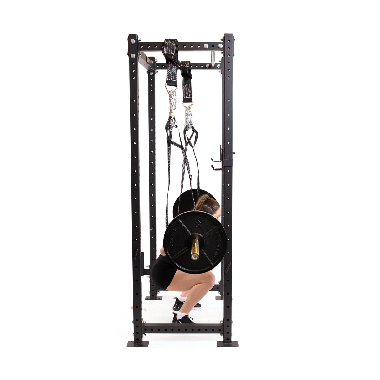 A person squats with a loaded barbell in a power rack, using Bells of Steel Suspension Spotter Straps And Bodyweight System for support. The setup is ideal for home gyms, with a plain white background.