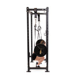 A person squats with a loaded barbell in a power rack, using Bells of Steel Suspension Spotter Straps And Bodyweight System for support. The setup is ideal for home gyms, with a plain white background.