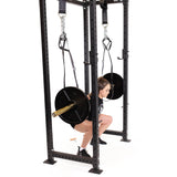 A person performs a low barbell squat inside a power rack using Bells of Steel Suspension Spotter Straps And Bodyweight System, facing sideways against a plain white background.